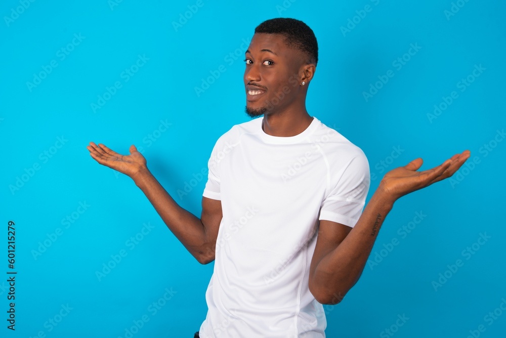 Careless attractive Handsome man wearing white T-shirt over blue background shrugging shoulders, oops. Careless attractive Handsome man wearing white T-shirt over blue background shrugging shoulders, oops.