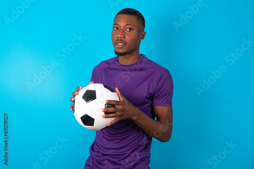 Business Concept - Portrait of Man wearing purple T-shirt holding a ball over blue background holding hands with confident face.