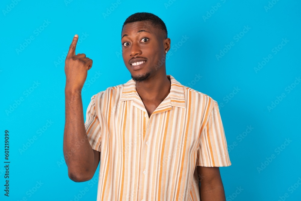 Handsome man wearing fashion shirt over blue background smiling and looking friendly, showing number one or first with hand forward, counting down Handsome man wearing fashion shirt over blue background smiling and looking friendly, showing number one or first with hand forward, counting down