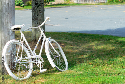 An adult bike painted white as a memorial site for a previous bicycle crash. The ghost bike is a symbol of memory and a reminder to share the road.  The ghost cycle is chained to a pole on a sidewalk. photo