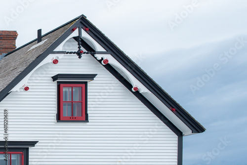 Exterior white wooden wall of horizontal clapboard siding vintage house with black and green trim. There's a small four pane glass window with red trim and a decorative gable roof. The sky is cloudy. photo