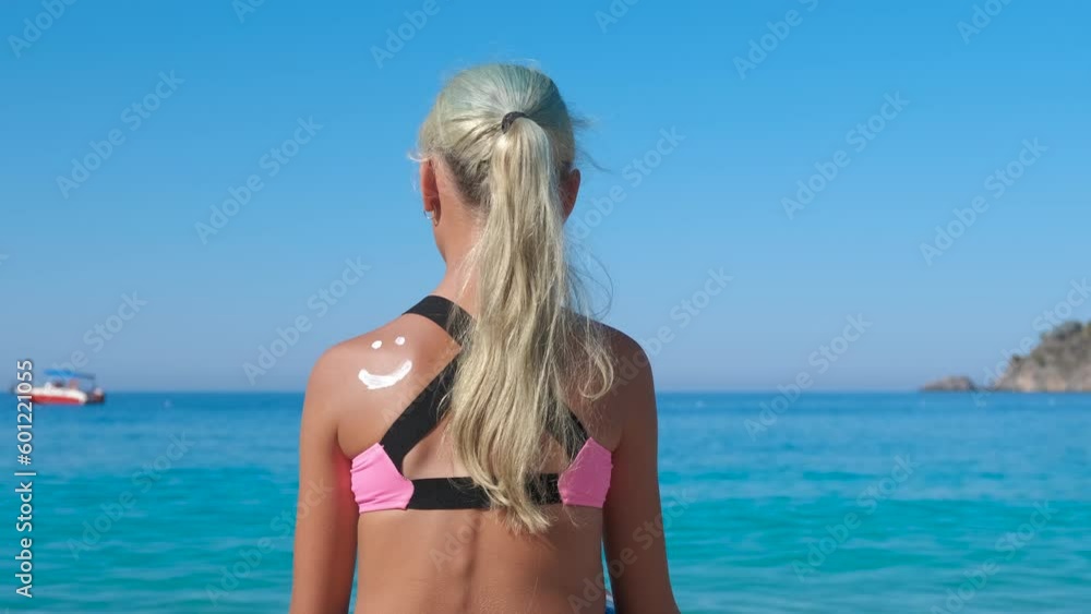 Girl preventing sunburn on shore. A young girl preventing the sunburn and makes a smile from lotion on her shoulder on the beach. Girl preventing sunburn on shore. A young girl preventing the sunburn and makes a smile from lotion on her shoulder on the beach.