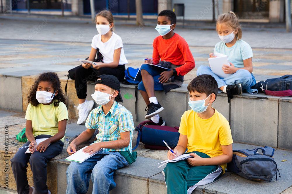 Group of schoolchildren in protective face masks having open air lesson during pandemic situation