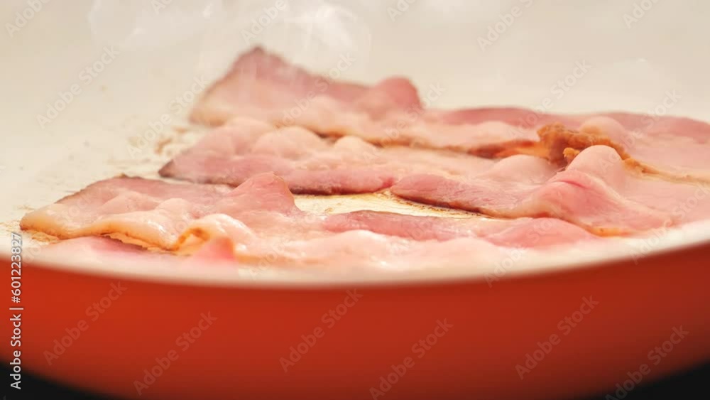 Smoky fried bacon.Bacon strips fry in an orange frying pan. 4k footage Smoky fried bacon.Bacon strips fry in an orange frying pan. 4k footage
