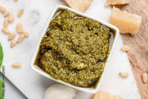 Board with bowl of delicious pesto sauce and ingredients, closeup