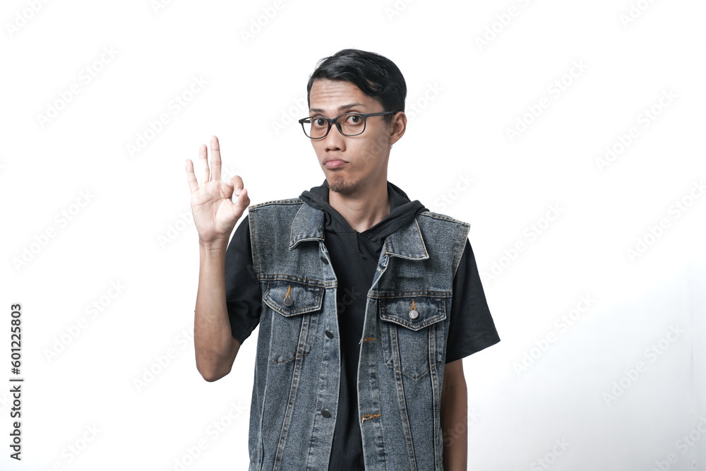 Asian man wearing sleeveless blue jean jacket giving ok or thumbs up sign that he agrees. Isolated white background Asian man wearing sleeveless blue jean jacket giving ok or thumbs up sign that he agrees. Isolated white background