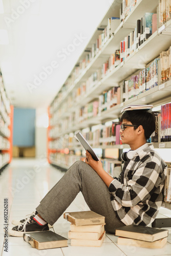 Handsome young student reading book on library floor at the university with books on his head and many books on the floor prepare for class assignment
