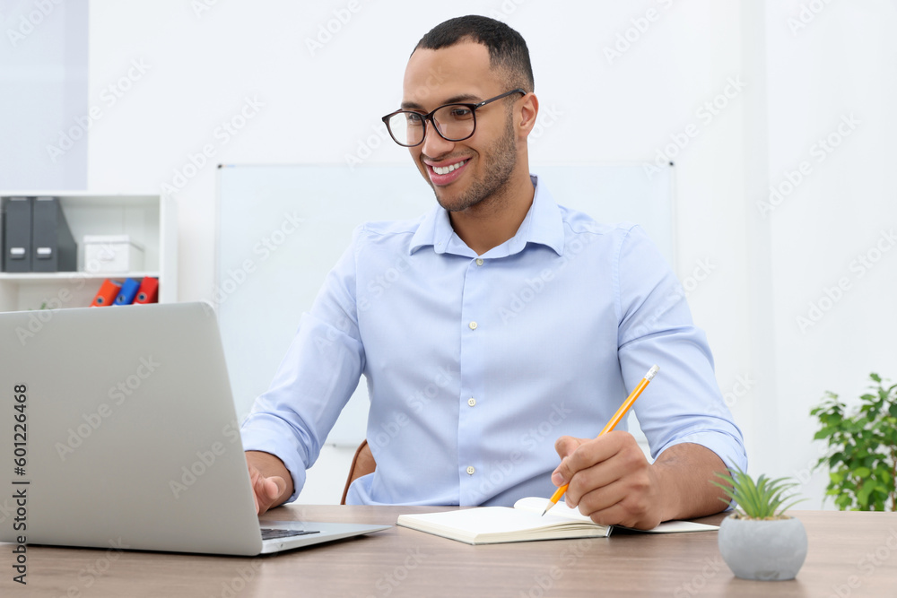 Happy young intern working with laptop at table in modern office Happy young intern working with laptop at table in modern office