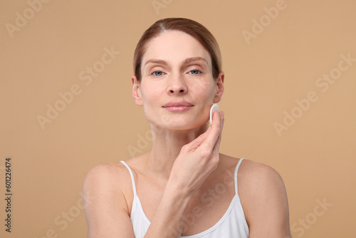 Beautiful woman removing makeup with cotton pad on beige background