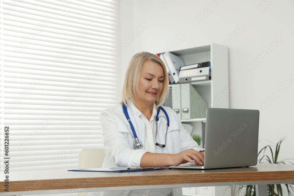 Doctor working on laptop at wooden table in clinic Doctor working on laptop at wooden table in clinic