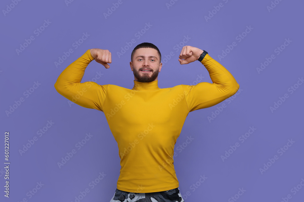Naklejka premium Handsome man showing muscles on purple background