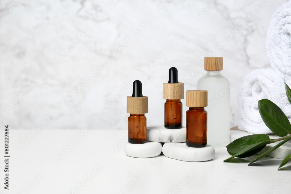 Bottles of essential oil, green leaves and spa stones on white table, space for text