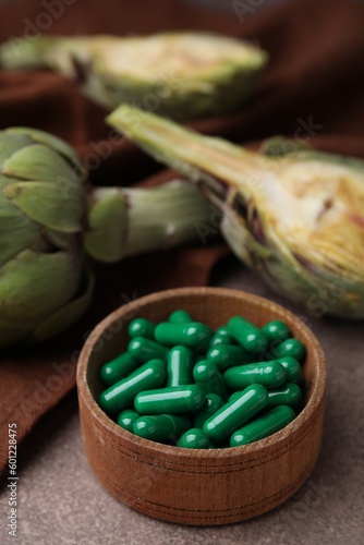 Bowl with pills and fresh artichokes on brown table, closeup