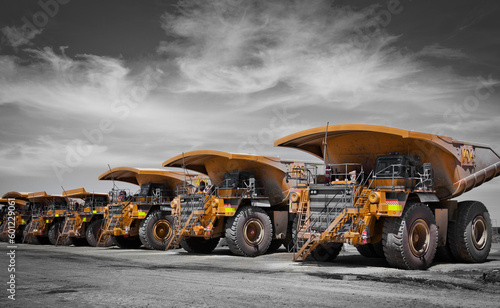 Massive yellow excavation trucks lined up. Used for transporting mine ore. Industrial transportation. Spot color yellow. All logos removed.