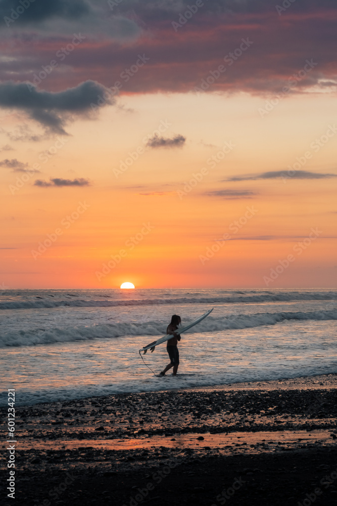 Silhouette of a surfer woman walking on a beach in Costa Rica during the sunset