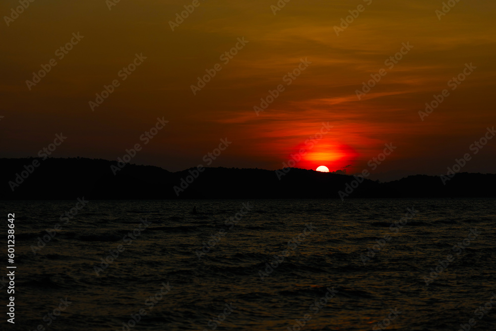 Beautiful blazing sunset landscape at dark sea and mountain with orange sky
