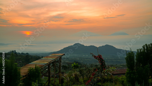 Beautiful reddish orange sunrise sky with mountain range and plantation on the foreground -  Mangli Sky View Tourist attraction on slope  Sumbing Mountain, Indonesia photo