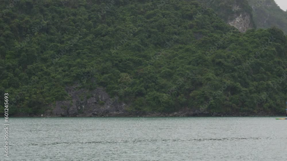 A scenic view of Ha Long Bay in Vietnam featuring water and a mountainous island. The camera pans right to reveal a tourist boat. A scenic view of Ha Long Bay in Vietnam featuring water and a mountainous island. The camera pans right to reveal a tourist boat.
