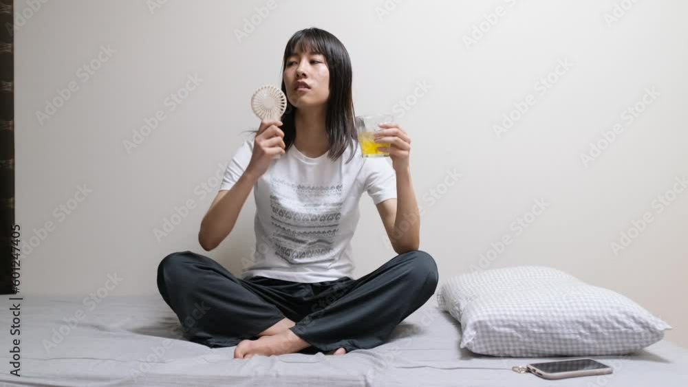 寝室でミニ扇風機の風にあたって涼む女性のズームインショット 寝室でミニ扇風機の風にあたって涼む女性のズームインショット