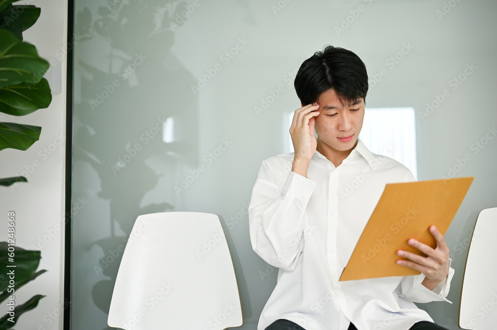 Confused Asian male candidate rechecked his resume while waiting for an interview. Confused Asian male candidate rechecked his resume while waiting for an interview.