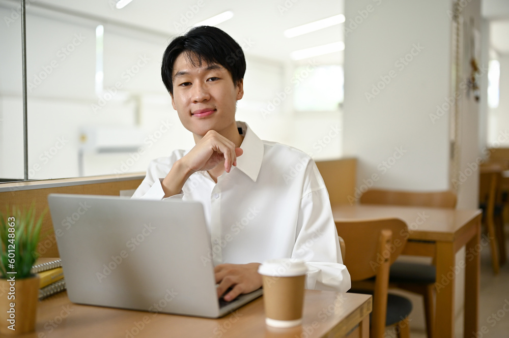 Smart Asian man sits in a coffee shop with his laptop and coffee cup on a table. Smart Asian man sits in a coffee shop with his laptop and coffee cup on a table.