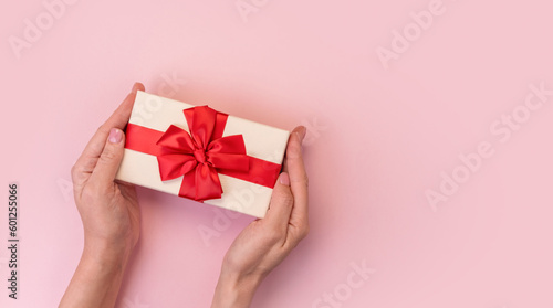 Hands holding gift box with red bow on pink background. Top view © kuzenkova