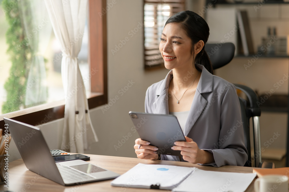 Young Asian businesswoman reading graphs and talking on phone with customers in office Young Asian businesswoman reading graphs and talking on phone with customers in office