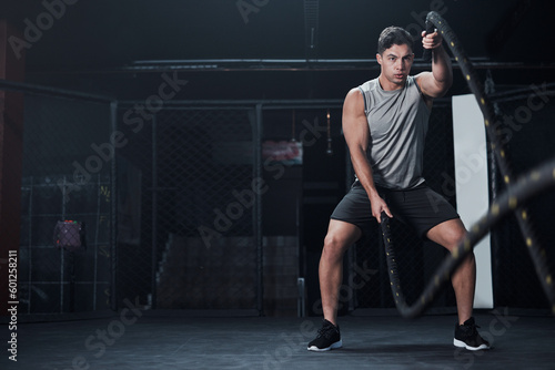 Fitness, battle ropes and man at the gym doing strength, cardio and challenge workout. Strong, energy and male athlete doing exercise or training with equipment for health and wellness in sports club photo