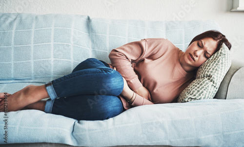 Woman, stomach ache or pain on home sofa with menstrual or period cramps in lounge. Sick, abdomen or colon problem of a female person with hands on tummy for constipation, digestion or virus photo