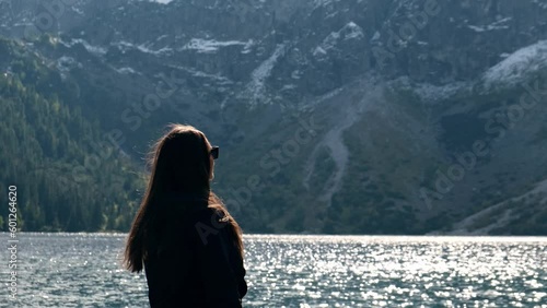 Young woman enjoying Tatra National Park, Poland. Tourist in Famous Mountains Lake Morskie Oko Or Sea Eye Lake In autumn. Snow covered mountain peaks on background. Blue water nature landscape 4k