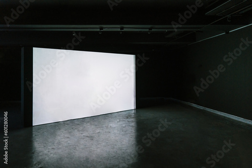 Empty room with blank mockup movie screen monitor standing in dark theater on black wall background. No people. Arts and entertainment concept.