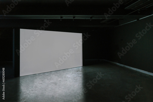 Empty room with blank mockup movie screen monitor standing in dark theater on black wall background. No people. Arts and entertainment concept.