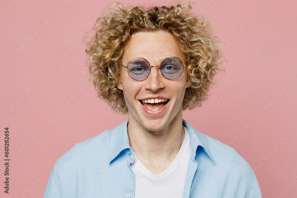 Close up young stylish happy smiling cheerful cool blond man wearing blue shirt white t-shirt sunglasses look camera isolated on plain pastel light pink background studio portrait. Lifestyle concept.