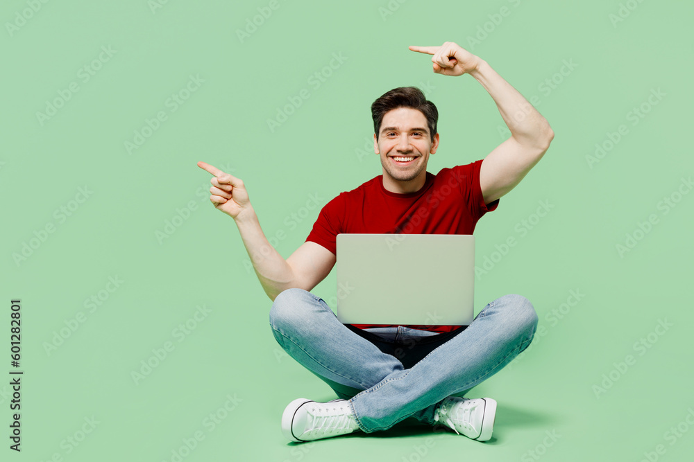Φωτογραφία Full body young IT man he wearing red t-shirt casual clothes hold use work on laptop pc computer point finger aside isolated on plain pastel light green background studio portrait