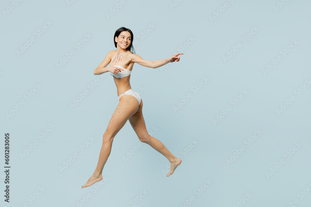 Full body side view young woman wear swimsuit jump high near hotel pool point index finger aside on area run isolated on plain pastel light blue background. Summer vacation sea rest sun tan concept.
