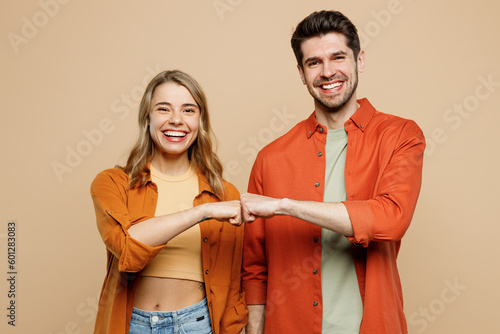 Young smiling happy buddies fun couple two friends family man woman wear casual clothes looking camera giving fist bumo together isolated on pastel plain light beige color background studio portrait.