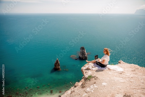 Freelance woman working on a laptop by the sea, typing away on the keyboard while enjoying the beautiful view, highlighting the idea of remote work. © svetograph