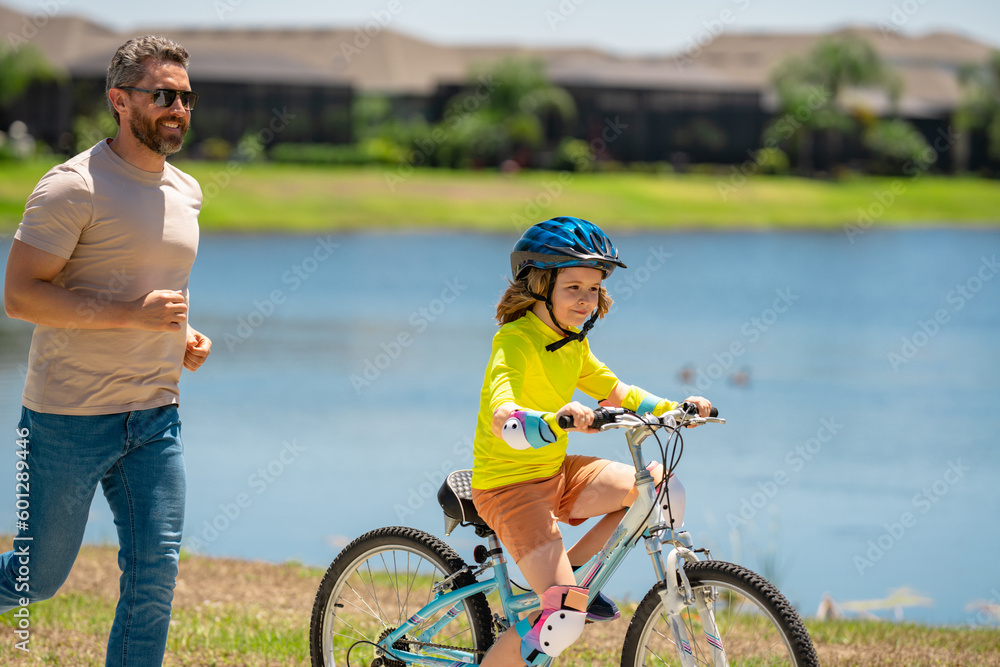 Happy Fathers day. Father and son in bike helmet for learning to ride bicycle at park. Father helping son cycling. Father and son on the bicycle on summer day. Kid son trying to ride bike with father.