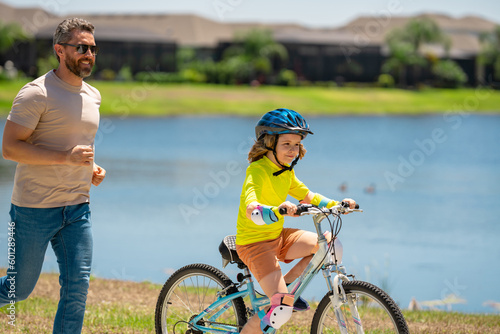 Happy Fathers day. Father and son in bike helmet for learning to ride bicycle at park. Father helping son cycling. Father and son on the bicycle on summer day. Kid son trying to ride bike with father.