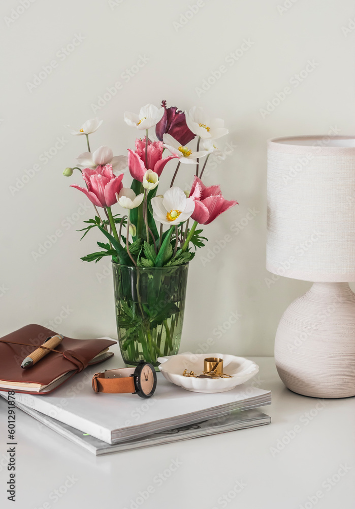 Cozy interior - a ceramic table lamp, a bouquet of spring flowers, women's accessories on a white marble countertop