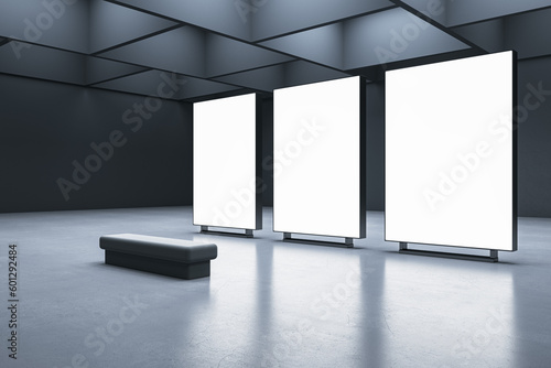 Perspective view on a bench on concrete floor in front of three blank white illuminated screens with place for your advertising text on dark wall background in gallery hall. 3D rendering, mock up