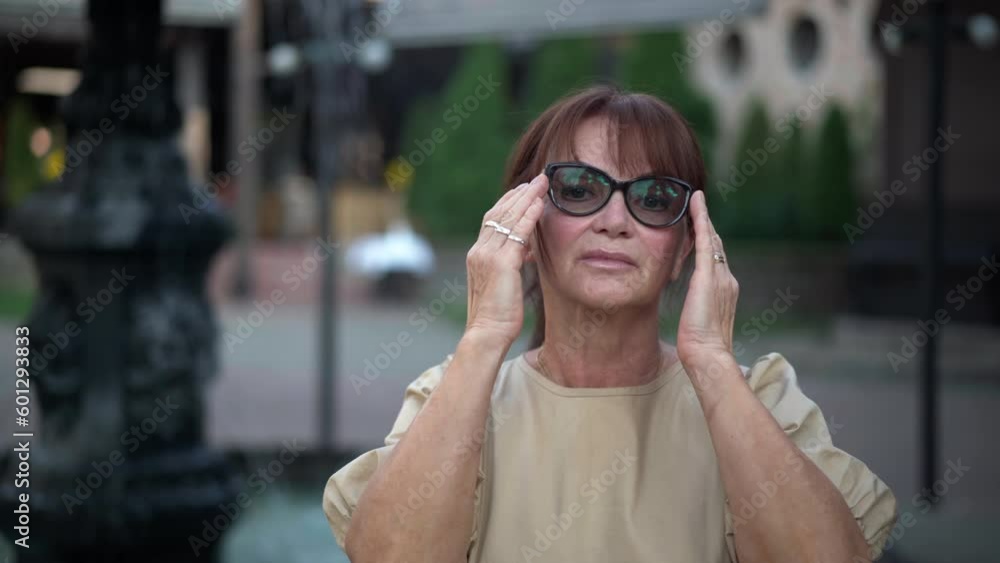 Caucasian woman in eyeglasses raising head looking at camera with confident facial expression. Portrait of beautiful mature lady posing at fountain in urban city park outdoors Caucasian woman in eyeglasses raising head looking at camera with confident facial expression. Portrait of beautiful mature lady posing at fountain in urban city park outdoors