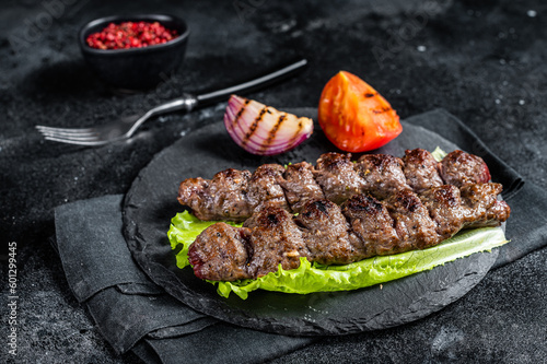Grilled Urfa kebab with tomato, salad and onion. Black background. Top view