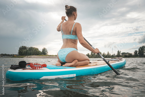 Caucasian woman is riding a SUP board on the river in city. Summer sport. © diy13