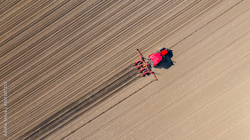 Aerial top view of tractor as dragging a sowing machine over agricultural field, farmland