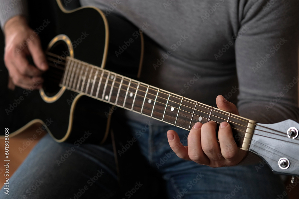 Playing the guitar. Strumming acoustic guitar. Musician plays music. Man fingers holding mediator. Man hand playing guitar neck in dark room. Unrecognizable person rehearsing, fretboard close-up