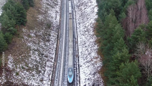 Aerial top down view on high speed express train passing forest on winter day