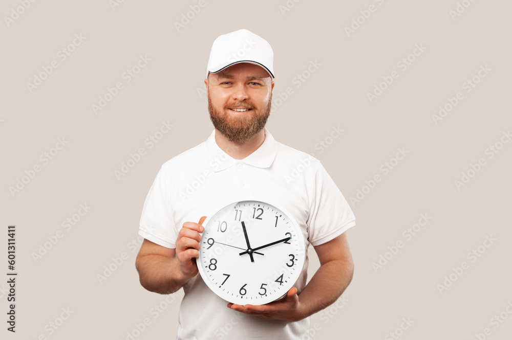 Smiling bearded delivery man wearing white uniform is holding a round clock because he is punctual. Smiling bearded delivery man wearing white uniform is holding a round clock because he is punctual.