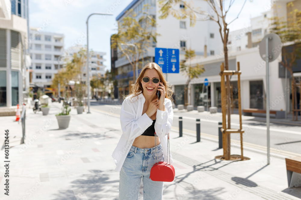 Image of beautiful stylish woman walking on city street on summer day and holding mobile phone. Cyprus, Nicosia