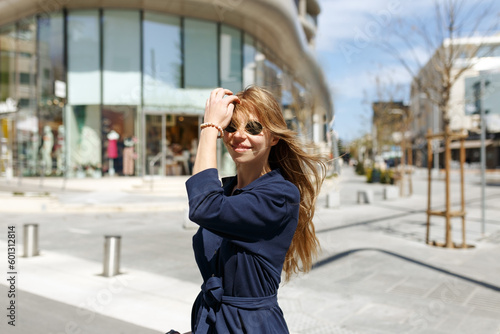 Shot of pretty young woman in dress crossing the street while holding the take away coffee and looking sideways